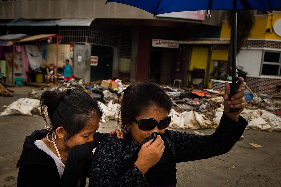 Residents of Tacloban City, Leyte province, Philippines cover their mouths as they pass dead bodies laying in the street on Tuesday, Nov. 19, 2013. Typhoon Haiyan caused widespread destruction, killing thousands and displacing millions. Photo by Erik M. Lunsford/LCMS