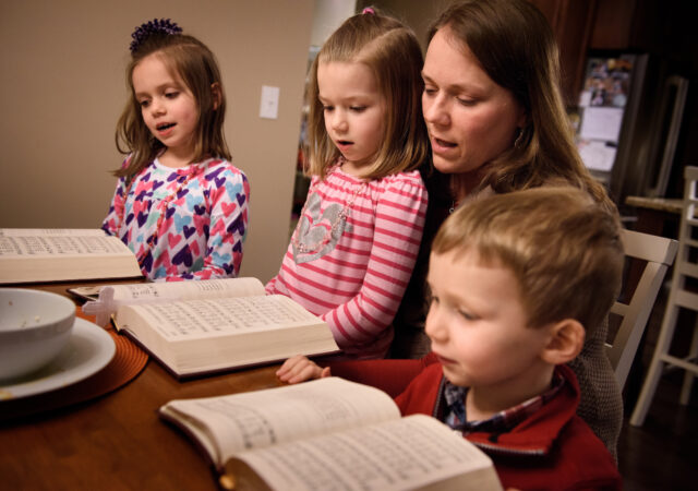 Laurie Vogt sings from the Lutheran Service Book with her children Elizabeth, Abigail (in lap) and Carl during an evening devotion with the Congregation at Prayer resource at their home on Sunday, Feb. 7, 2016, in Menomonee Falls, Wis. LCMS Communications/Erik M. Lunsford