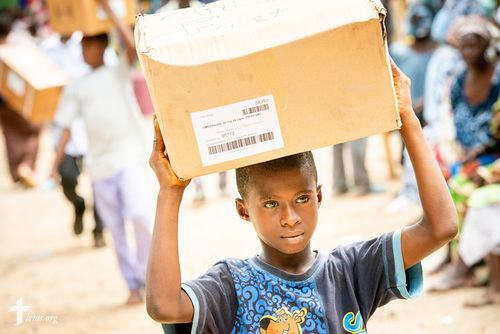 A boy walks medication delivered to the clinic site on the first day of the LCMS Mercy Medical Team on Monday, May 7, 2018, in the Yardu village outside Koidu, Sierra Leone, West Africa. LCMS Communications/Erik M. Lunsford